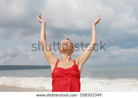 Attractive young woman stretching her arms up wile standing on a golden sand beach.
