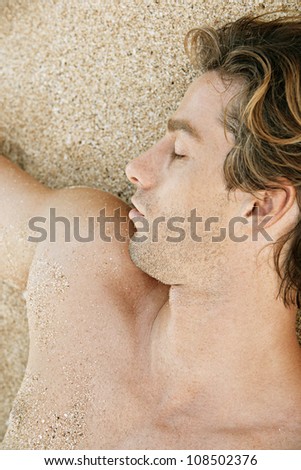 Over head close up view of an attractive man sunbathing on a beach.