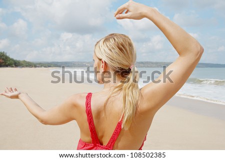 Rear view of a young woman practicing martial arts while standing by the shore on a golden sand beach.