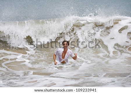Attractive young man running out of the wild ocean, with a large wave behind him.
