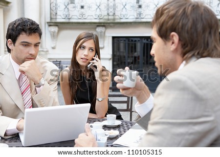 Three business people having a meeting at a coffee shop's terrace and using technology, outdoors.