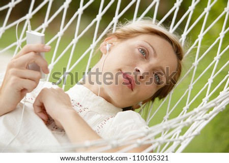 Young beautiful woman laying down on a hammock while on vacations in a tropical destination hotel\'s garden and listening to music with her earphones and smiling.