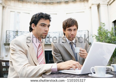 Two attractive businessmen having a meeting while having coffee in a coffee shop\'s terrace, outdoors.