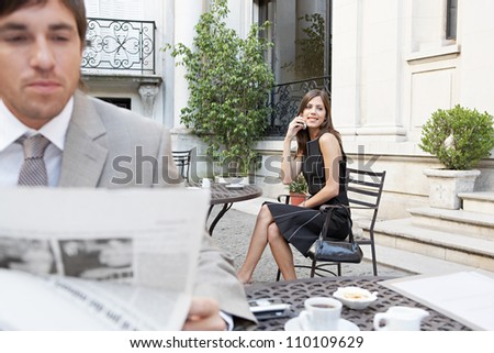 Two business people in a classic building\'s terrace reading the newspaper and talking on the cell phone.