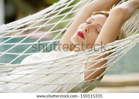 Young attractive woman laying down on a white hammock in a garden, while on vacations.