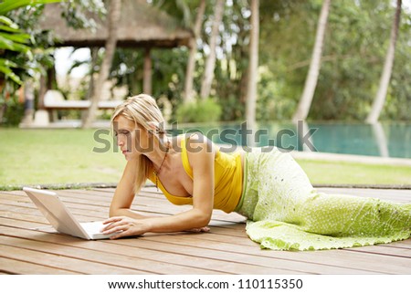 Attractive woman using a laptop computer in a hotel tropical garden near a swimming pool.