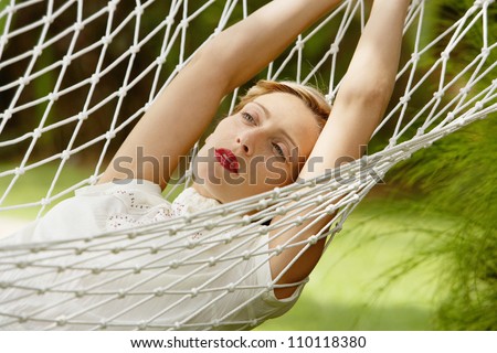 Young attractive woman laying and relaxing on a white hammock in a tropical garden.