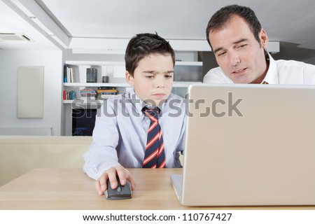 Father helping his son with his homework while sharing a laptop pc computer at home.