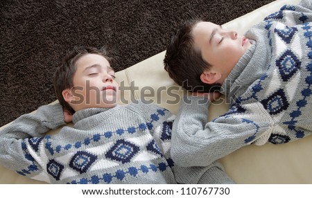 Two identical twin brothers sleeping on a white leather couch while wearing identical jumpers.