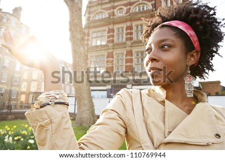 Beautiful young black woman holding the sun between her fingers at sunset while visiting London city.