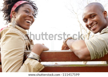 Side view of an african american couple sitting on a wooden bench against the sky, laughing together.