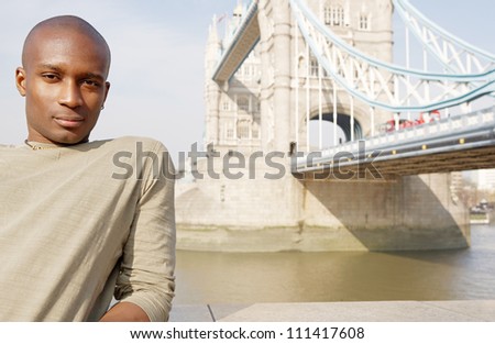 Attractive african american man standing by Tower Bridge in London being thoughtful and contemplating the city.