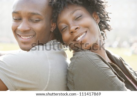 Young african american couple sitting back to back while visiting London on vacation, smiling and in love.