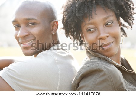 Young african american couple sitting back to back while visiting London on vacation, smiling at camera.