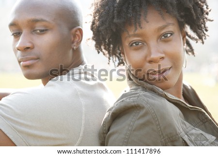 Young attractive african american couple sitting back to back in a city park while on vacation, smiling happy.