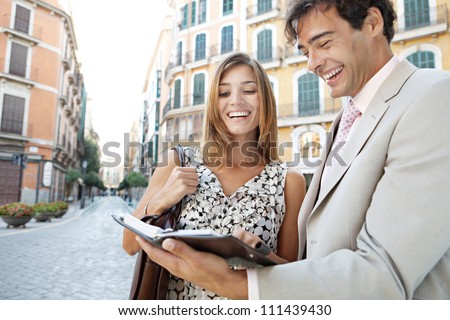 Businessman and businesswoman laughing while having a meeting outdoors, in a classic city.