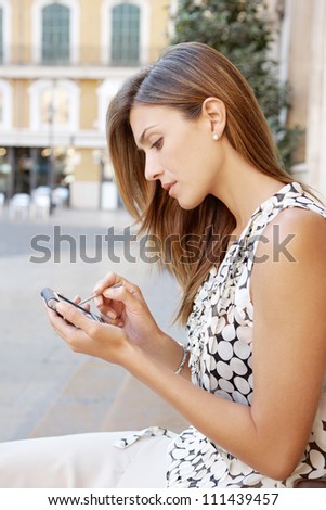 Profile view of an attractive businesswoman sitting down in a classic city\'s square using a tablet smart phone.