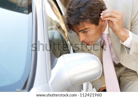 Attractive young businessman grooming using a car\'s reversing mirror to tidy his hair up, preparing for a business meeting.