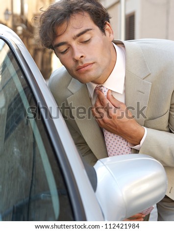 Attractive young businessman grooming using a car\'s reversing mirror to tidy his tie knot, preparing for a business meeting.