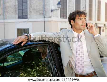 Businessman using a cell phone to make a phone call while standing by a car in the city.