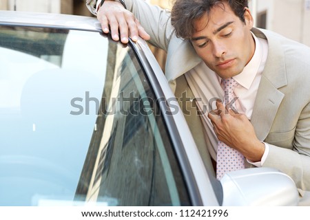 Attractive young businessman grooming using a car\'s reversing mirror to tidy his tie knot, preparing for a business meeting.
