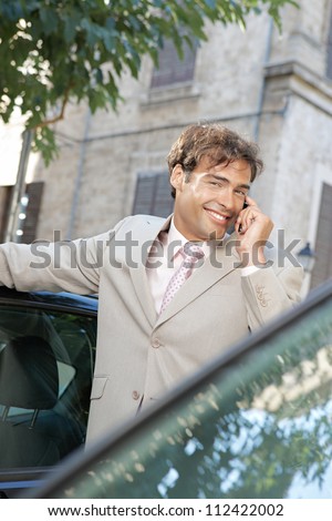 Businessman using a cell phone to make a phone call while standing some cars in the city, smiling.