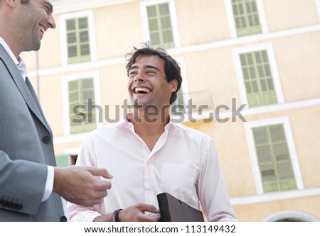 Portrait of two businessmen having a conversation while standing next to a classic building in the city, laughing.