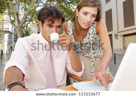 Business colleagues looking at a laptop screen while having a meeting in a coffee shop terrace, outdoors.