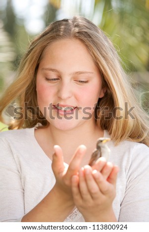 Close up portrait of a young teenage girl holding a baby bird in her hands, smiling.