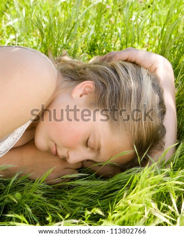 Close up  view of a teenage girl sleeping while laying down on long green grass in a garden.