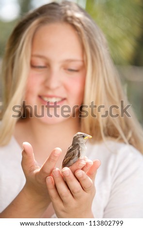 Close up portrait of a young teenage girl holding a baby bird in her hands, smiling.