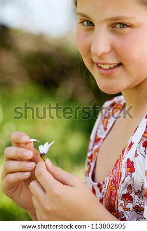 Young teenager pulling petals off a daisy flower, playing at love me love me not, smiling.