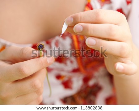 Young teenager pulling petals off a daisy flower, playing at love me love me not, close up.