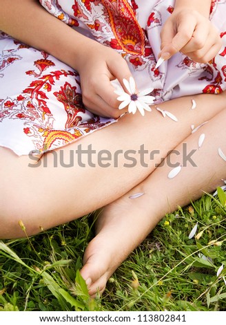 Over head view of a young teenager pulling petals off a daisy flower, playing love me love me not while sitting on a long green grass garden.