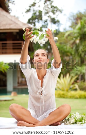 Attractive young woman offering and holding tropical flowers in her hands above her head, in an exotic spa garden.