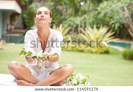 Attractive young woman offering and holding tropical flowers in her hands, in an exotic spa garden.