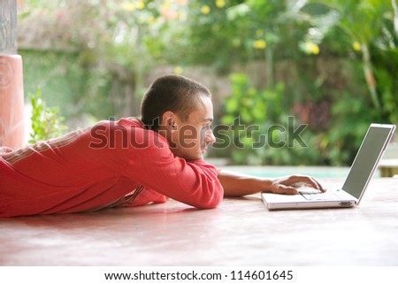 Attractive young man using a laptop computer while laying down in a tropical hotel garden.