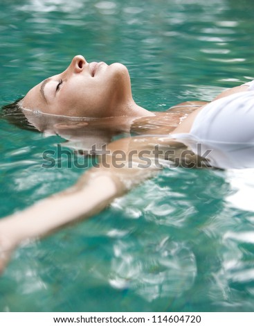 Close up view of an attractive young woman floating on a spa\'s swimming pool, smiling.