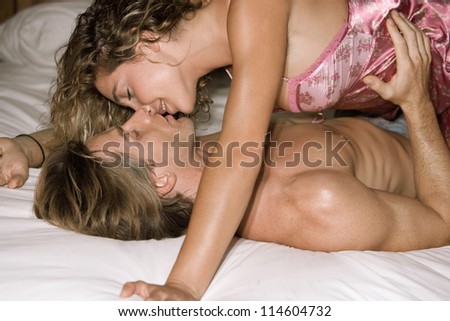 Attractive couple of lovers in bed being intimate with each other and kissing.