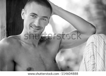 Black and white close up portrait of a young attractive man relaxing on a lounger while on vacation in a tropical destination.