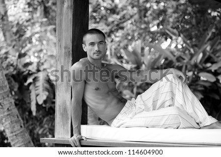 Black and white portrait of a young attractive man relaxing on a sun lounger while on vacation in a tropical destination.