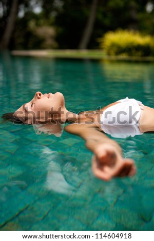 Side view of an attractive young woman floating on a swimming pool, smiling.