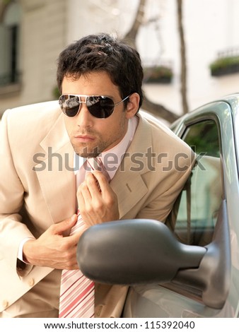 Close up view of an attractive businessman grooming himself using a car mirror outdoors, tightening his tie knot.