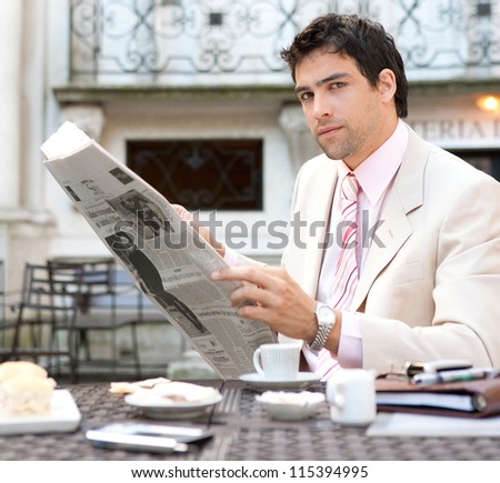 Attractive businessman reading the newspaper while having breakfast in an elegant luxury coffee shop, outdoors.