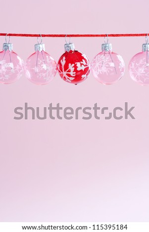 Small pink and red bar-balls Christmas tree ornaments hanging aligned on a red string against a pink background, panoramic format.