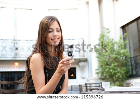 Portrait of a beautiful businesswoman using a cell phone while sitting in a classic coffee shop, smiling outdoors.