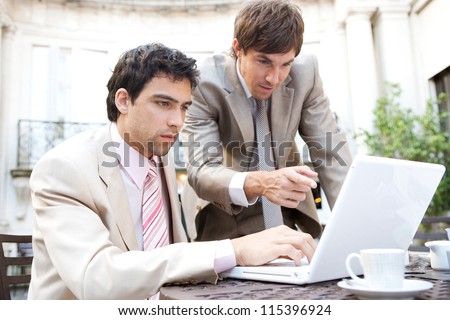 Two businessmen focused on having a meeting while sitting in a classic coffee shop terrace, using a laptop computer.