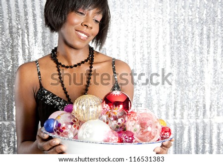 Close up portrait of an attractive black woman holding a dish full of christmas bar balls against a silver sequins background.