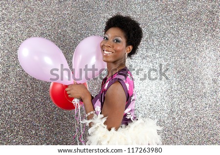 Attractive young black woman holding pink and red balloons against a silver glitter background, smiling.