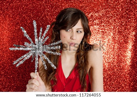 Attractive young woman holding a large christmas star while standing in front of a red glitter background with a thoughtful expression.